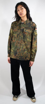 Full-body view of female model wearing fitted German surplus Flecktarn shirt, demonstrating tailored silhouette and camouflage pattern details.