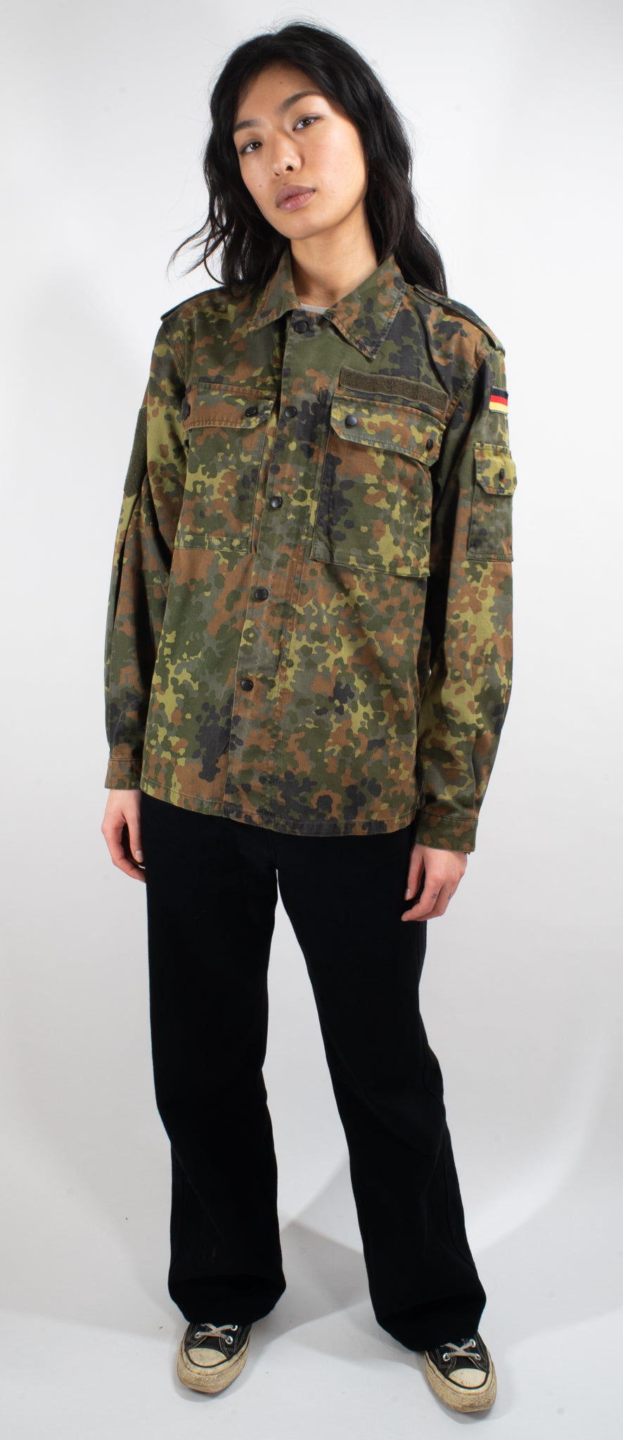 Full-body view of female model wearing fitted German surplus Flecktarn shirt, demonstrating tailored silhouette and camouflage pattern details.