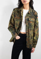 Model wearing genuine German Army Flecktarn shirt, showing front zipper, snap-stud storm flap, and integrated German flag shoulder patch.