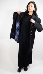 Woman displaying the interior of a black German Navy peacoat, revealing the removable blue plaid liner and quality construction.
