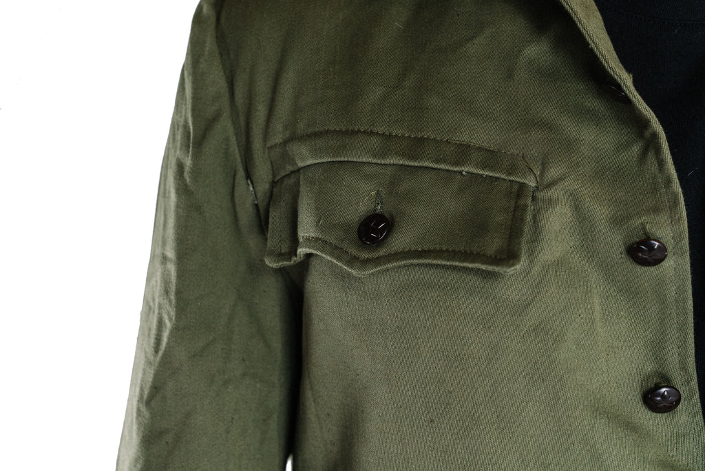 Detailed view of a scalloped chest pocket with an embossed pewter-colored socialist star button.
