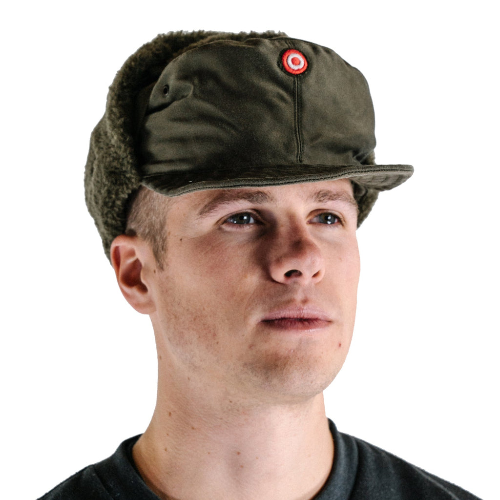 Austrian Army KAZ 75 winter cap worn by a model, featuring a rigid visor, windproof olive drab shell, and red-white-red national cockade.