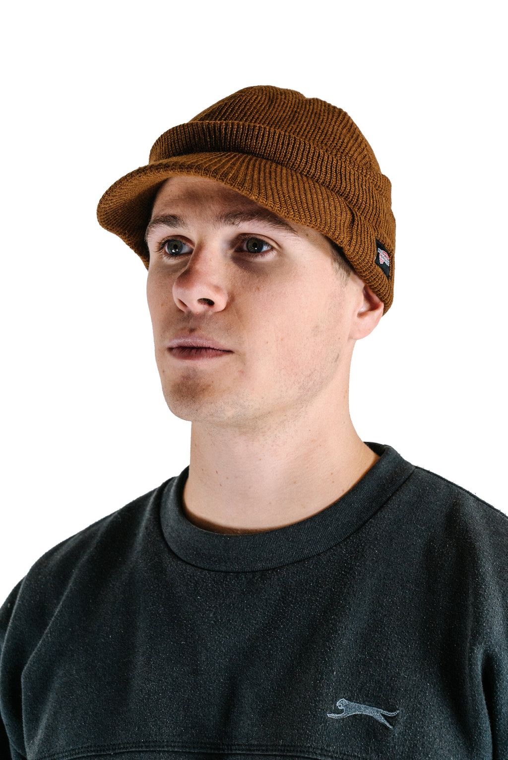 A model wears a brown ribbed knit Radar beanie by Red Wing Shoes, featuring a short brim and a small branded side tag.