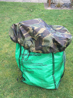 A Dutch Army waterproof Bergen cover protecting a green garden waste bag from rain while stored outdoors.
