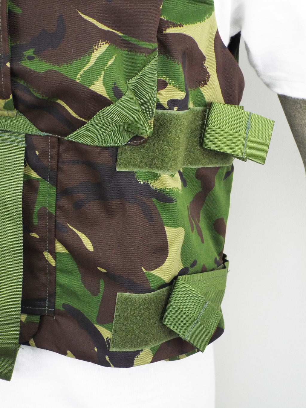 Side profile of the British DPM woodland camo flak vest, showing the adjustable green Velcro side straps designed for a secure torso fit.
