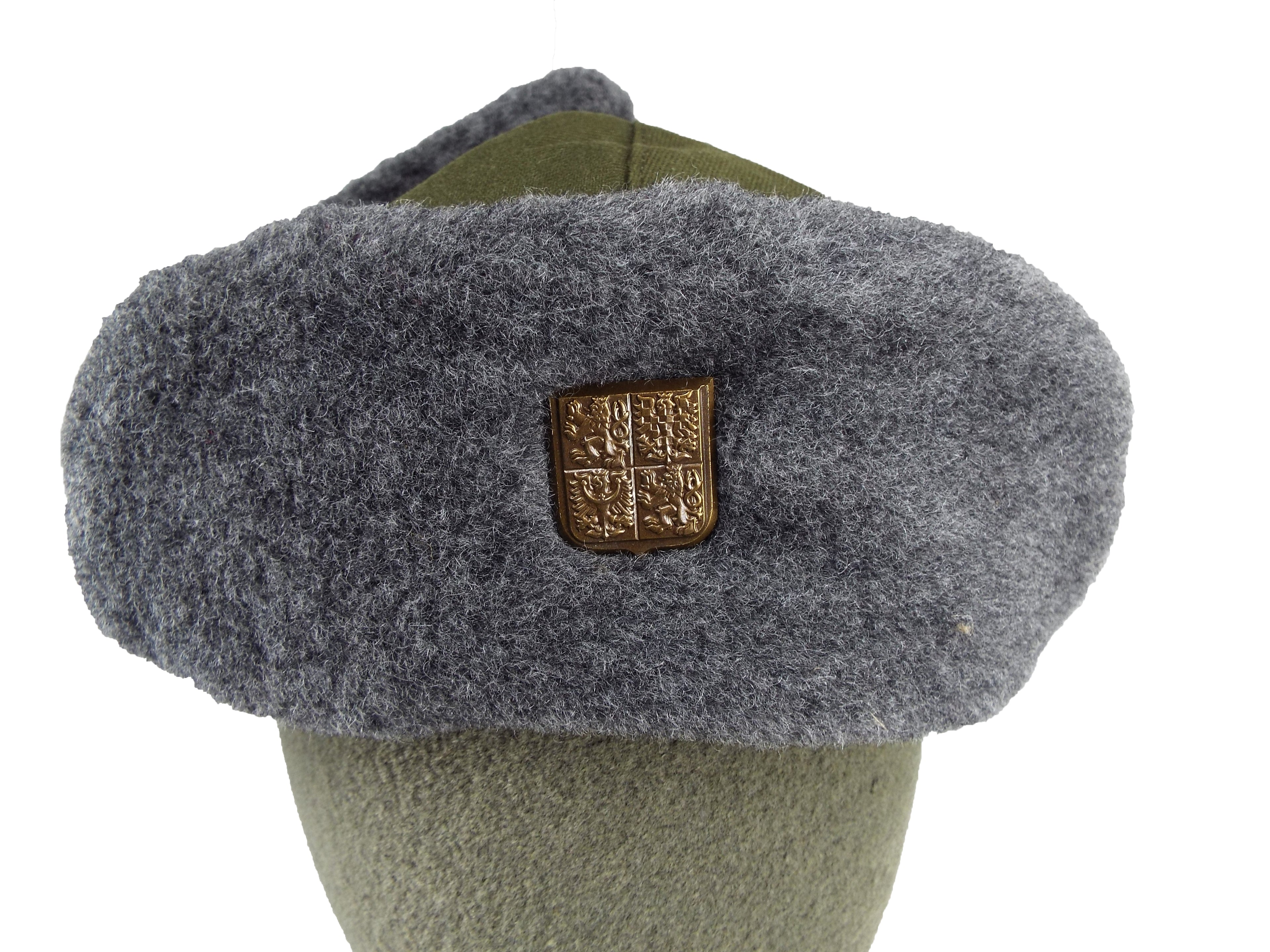 Close-up of the Czech Ushanka front with a detailed look at the metallic coat of arms badge fixed to the synthetic fur.