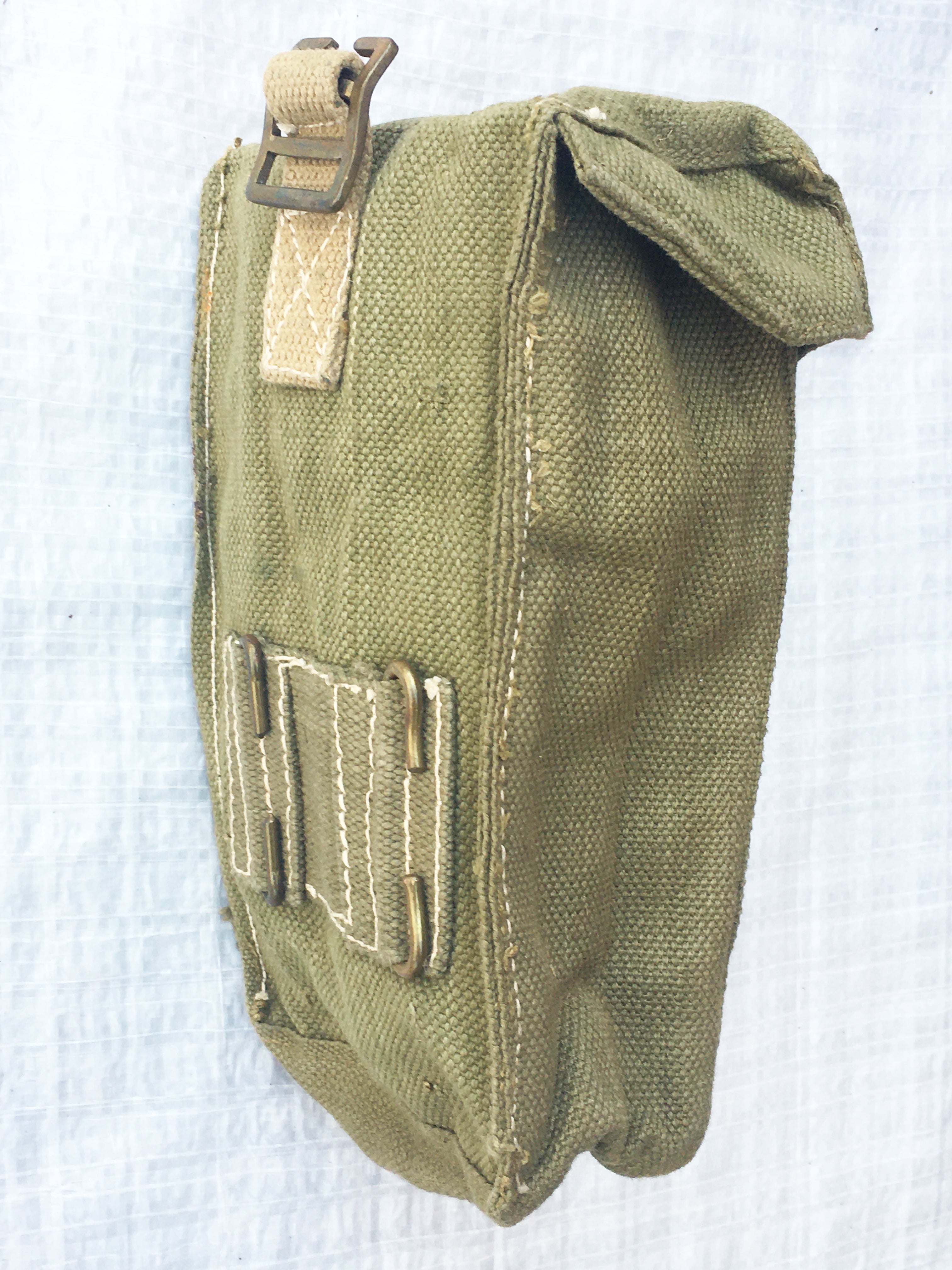 Angled rear view of a green military ammo pouch showing belt attachment hooks and reinforced cotton stitching.