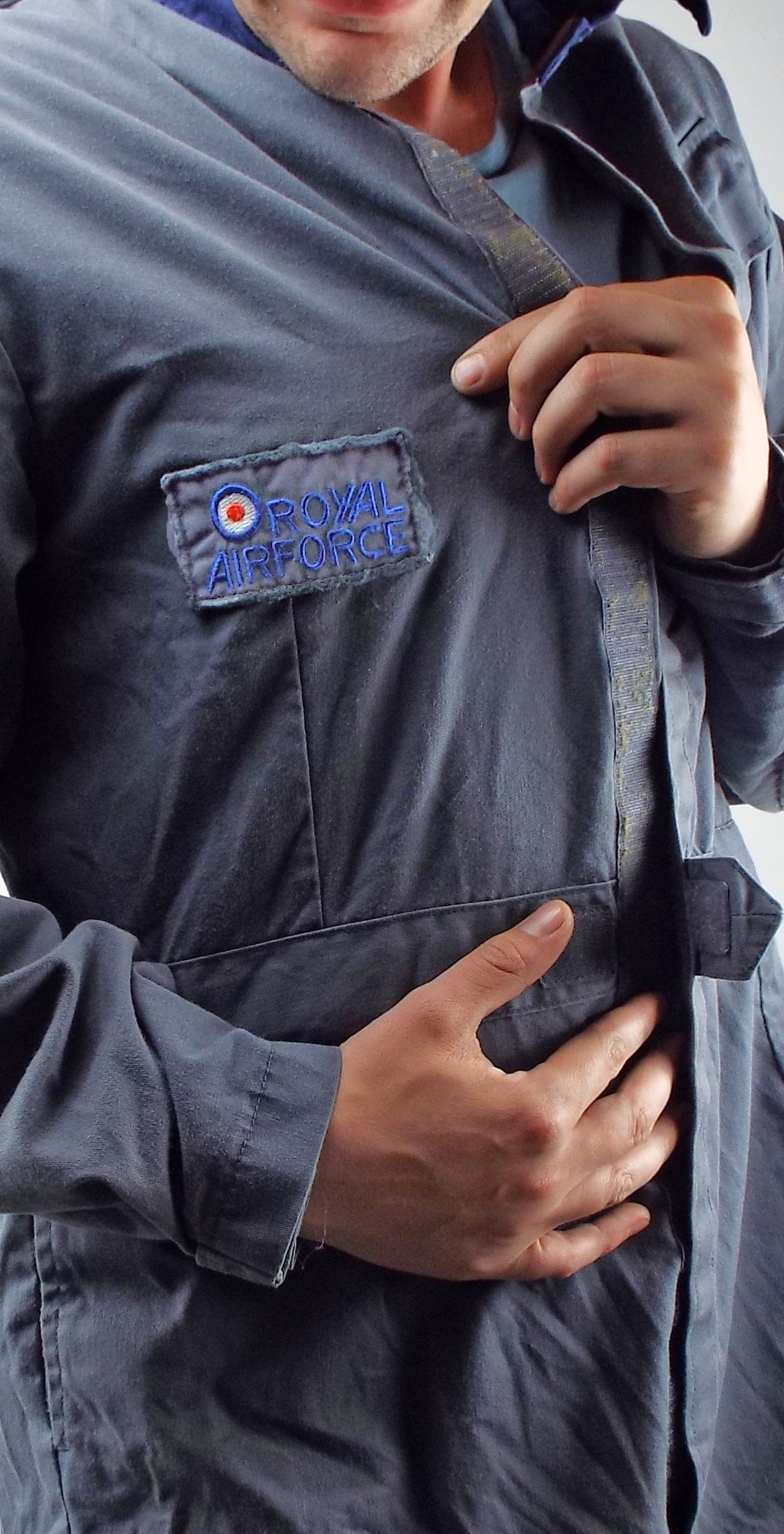 Detailed close-up of the Royal Air Force embroidered patch with red, white, and blue roundel on the chest of the blue/grey military overalls.